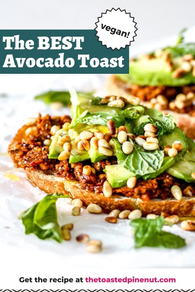 This is a side view of a slice of toast topped with harissa pesto, avocado, fresh herbs, and toasted pine nuts. The piece of toast sits on a white piece of parchment paper with another avocado toast blurred in the background. Text overlay reads "the best avocado toast vegan!"