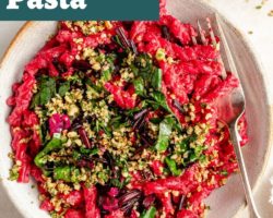 This is an overhead image of a shallow bowl with hot pink beetroot pasta topped with sautéed greens and a nutty mixture on top. A fork dips into the bowl and leans against the right side of the dish. Another bowl with pasta is to the top right corner of the image. A small bowl with nutty gremolata is to the top left corner of the image. Text overlay reads "beetroot pasta vegan!"