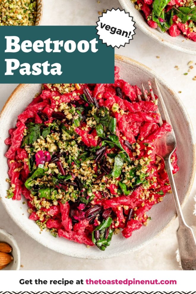 This is an overhead image of a shallow bowl with hot pink beetroot pasta topped with sautéed greens and a nutty mixture on top. A fork dips into the bowl and leans against the right side of the dish. Another bowl with pasta is to the top right corner of the image. A small bowl with nutty gremolata is to the top left corner of the image. Text overlay reads "beetroot pasta vegan!"