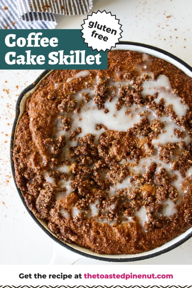 This is an overhead image of a white skillet with a coffee cake topped with a crumble streusel and vanilla glaze icing. The skillet sits on a white counter and a grey and white pinstripe tea towel is to the top left corner. The skillet and counter is sprinkled with cinnamon. Text overlay reads "gluten free coffee cake skillet."