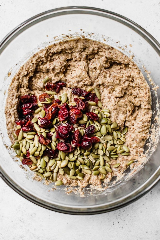 This is an overhead image of a glass bowl with flaxseed bread batter in it. The batter has dried cranberries and pumpkin seeds on the top of it.