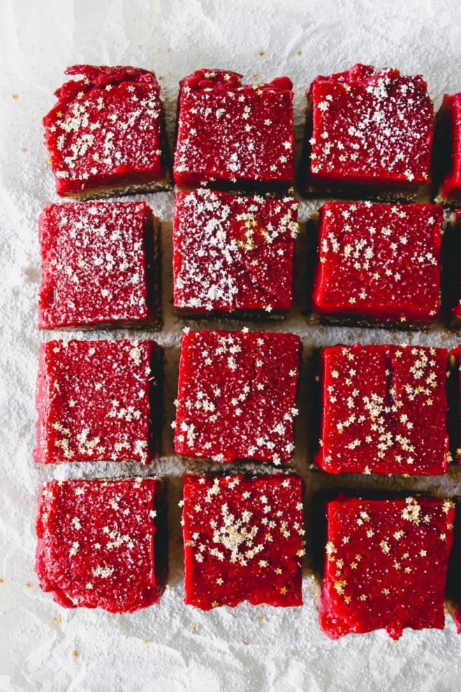 This is an overhead image of cranberry lemon bars on a white piece of parchment paper. The bars are sprinkled with powdered sugar and gold star sprinkles.