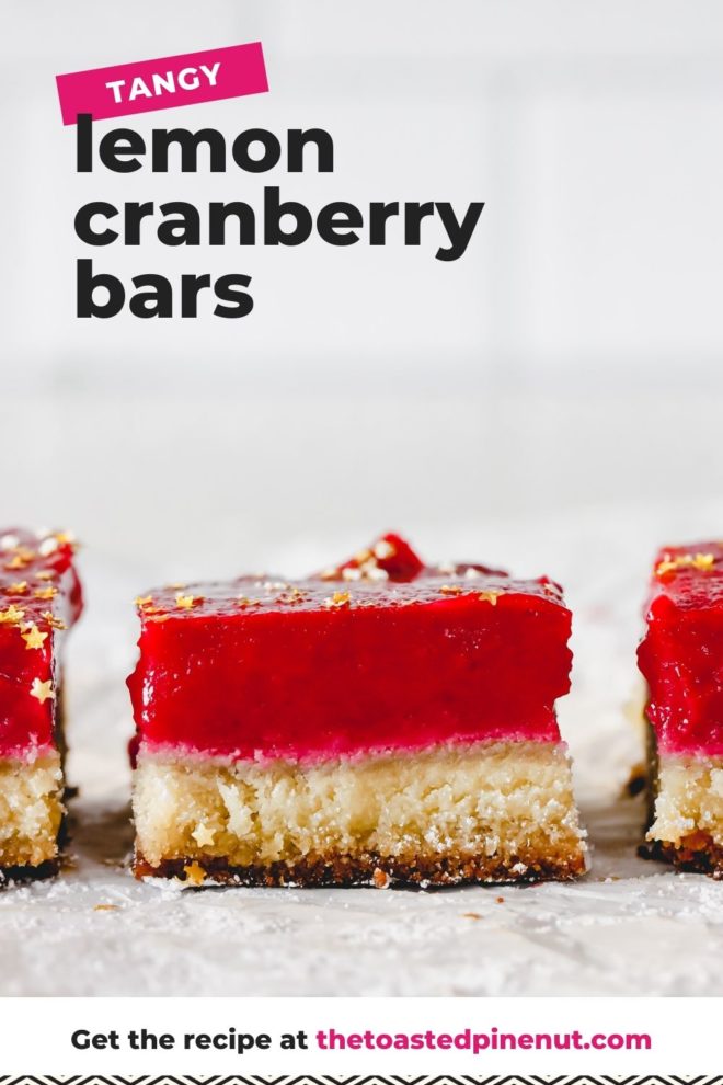 This is a side view of a lemon cranberry bar with more bars on either side of it. The bars sit on a white piece of parchment paper with a bite background. The cranberry lemon bars have a shortbread base and a bright magenta cranberry topping. The bars are topped with gold star sprinkles. Text overlay reads "tangy lemon cranberry bars."