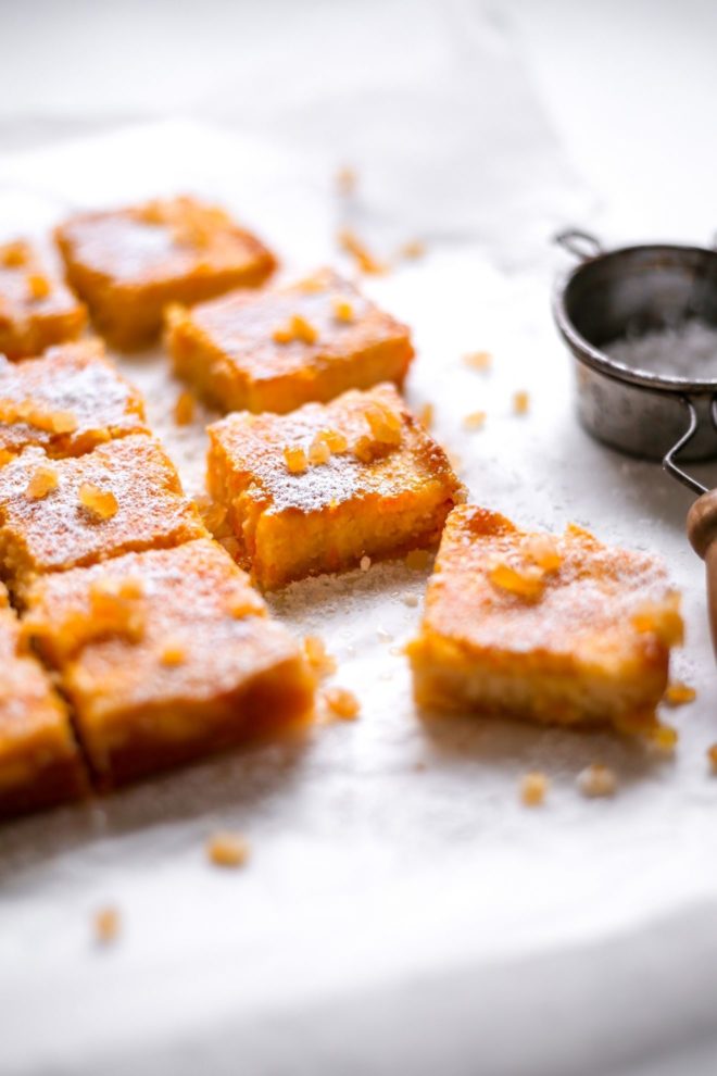 This is a side view of orange pie bars on a white piece of parchment paper. The orange bars are topped with candied oranges and powdered sugar.