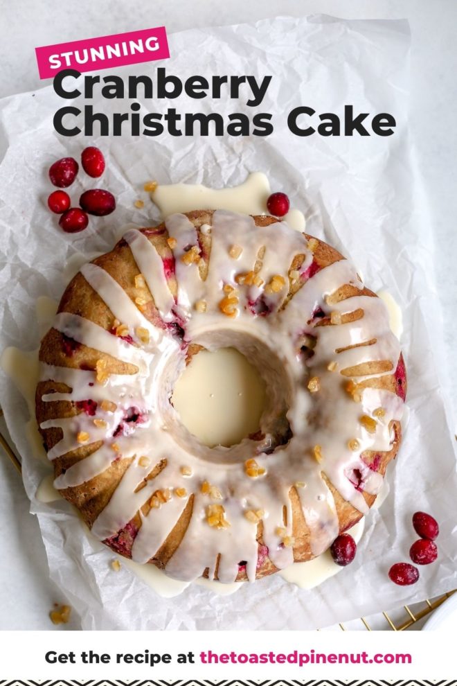 This is an overhead image of a cranberry orange cake glazed with a white icing and candied orange pieces. The cake sits on a white piece of parchment paper on a cooling rack. The cooling rack sits on a white surface. A few fresh cranberries are sitting on the parchment paper next to the cake. Text overlay reads "stunning cranberry christmas cake."