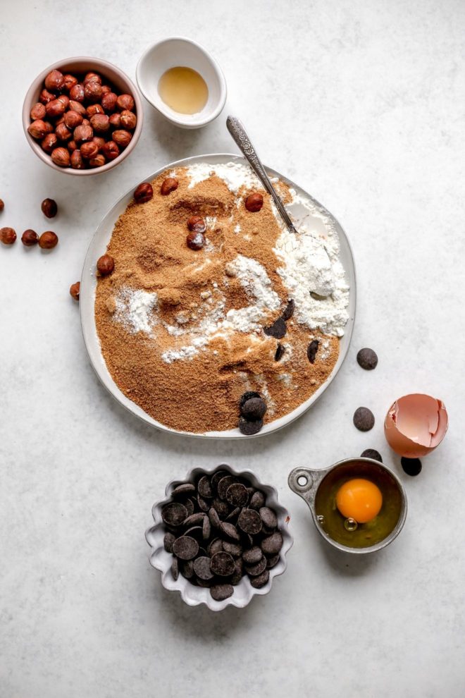 This is an overhead image of a few small bowls and a large plate containing ingredients to make chocolate hazelnut biscotti.