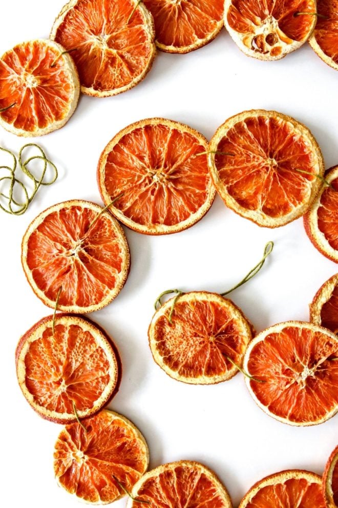 This is an overhead image of dried orange slices strung together with green string. The orange garland is arranged in a spiral on a white counter.