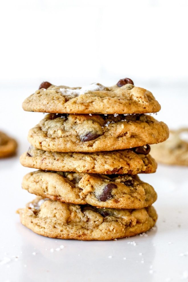 This is a stack of five sourdough cookies with chocolate chips and marshmallows in it. The stack sits on a white counter with more cookies blurred in the background.