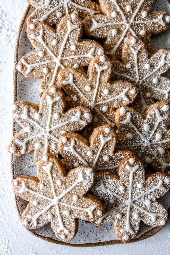 This is an overhead image of a rectangle plate with snowflake cutout cookies. The cookies are iced with a vanilla royal icing and sprinkled with powdered sugar.