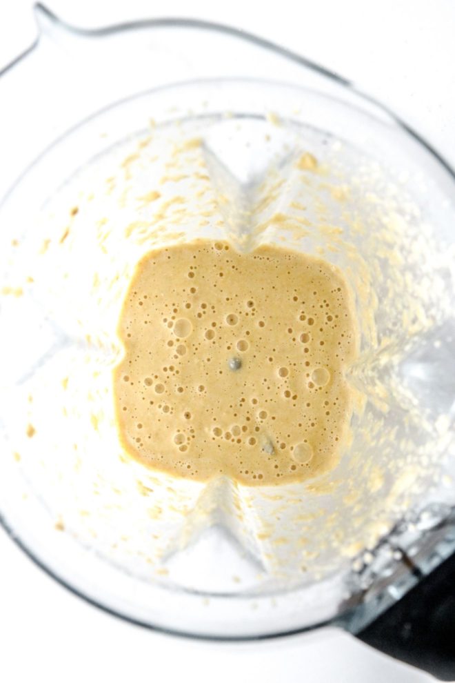 This is an overhead image in a blender on a white counter. Inside the blender is blended oatmeal with some bubbles in it.
