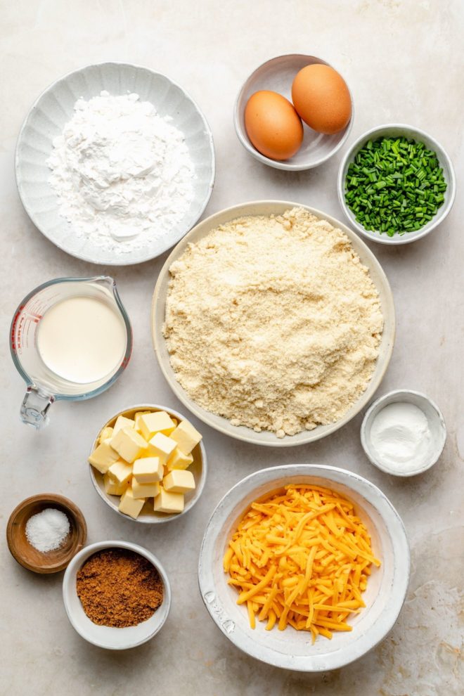 This is an overhead image of ingredients to make cheese and chive scones. The ingredients sit on a white surface.