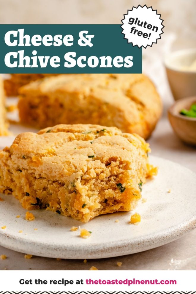 This is a side view of a cheese and chive scone with a bite taken out of it. The scone sits on a white plate which is sitting on a beige surface. More scones are blurred in the background. Text overlay reads "cheese & chive scones gluten free!"