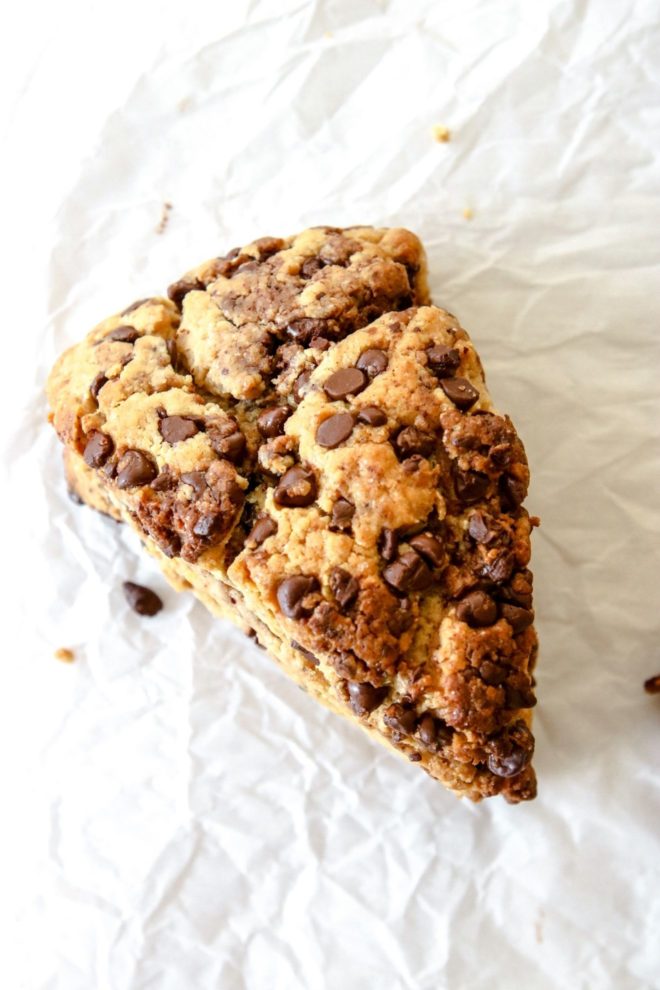 This is an overhead image of a single chocolate chip scone on a white piece of parchment paper. Text overlay reads:delicious peanut butter sourdough scones."