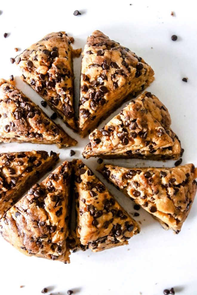 This is an overhead image of raw peanut butter chocolate chip scone dough cut into triangles. The scones are arranged in a circle and sit on a white counter with a few min chocolate chips around the triangles.