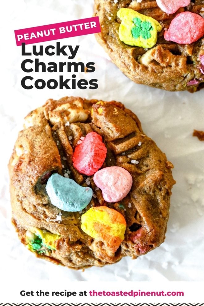 This is an overhead image of a peanut butter cookie topped with colorful lucky charms marshmallows. The cookie sits on a white piece of parchment paper with another cookie in the right top corner of the image. Text overlay reads"peanut butter lucky charms cookies."
