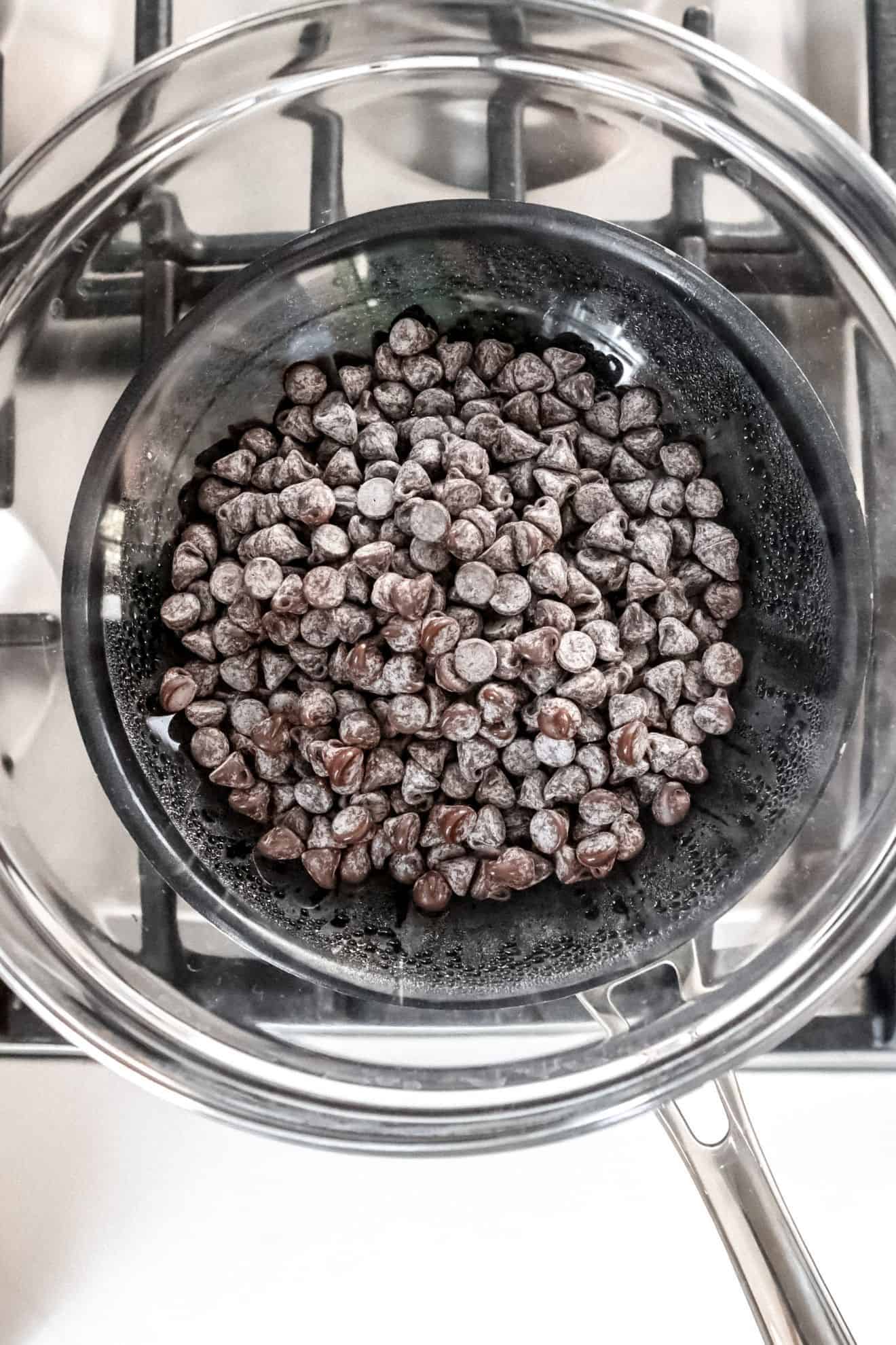 This is an overhead image of a pot on a stove. On top of the pot is a glass bowl with chocolate chips.