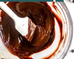 This is an overhead image of a glass bowl with melted chocolate. A spatula is in the bowl with the melted chocolate. The glass bowl sits on a white counter with more chocolate chips scattered around it. Text overlay reads "How to Melt Chocolate Chips two 2 ways!"
