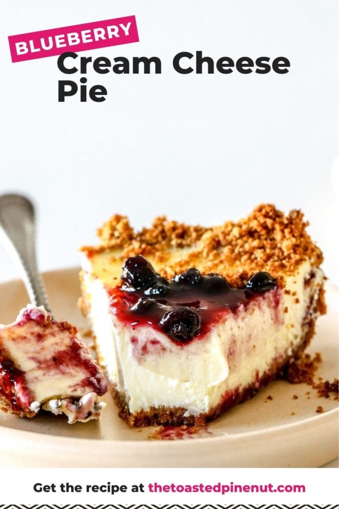 This is a side view of a slice of cream cheese pie. The slice is on a small beige plate and is topped with blueberry jam. A fork is taking off a bite of the pie and leaning on the side of the plate. The plate sits on a white counter with a white background. Text overlay reads "blueberry cream cheese pie."
