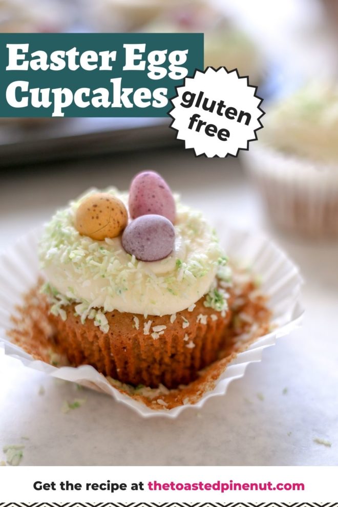 This is a side view of a vanilla cupcake with the liner peeled back. The cupcake sits on a light grey surface with more cupcakes blurred in the background. The cupcake is topped with vanilla frosting, light green coconut, and candy eggs. Text overlay reads "easter egg cupcakes gluten free."