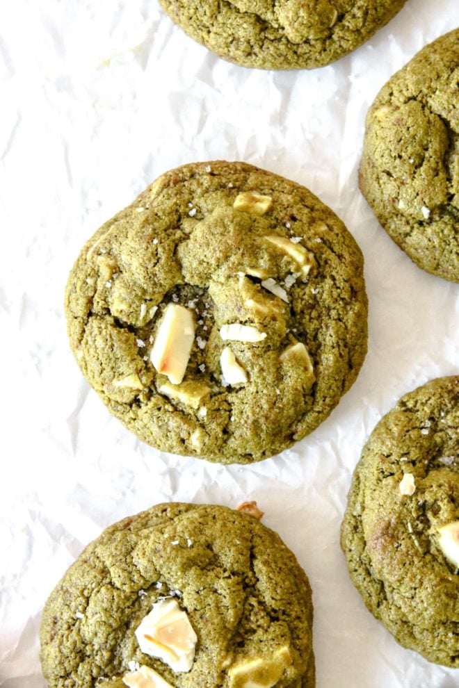This is an overhead image of green cookies with white chocolate cunks on top. The cookies are sprinkled with some flakey salt and sitting on a white piece or parchment paper.