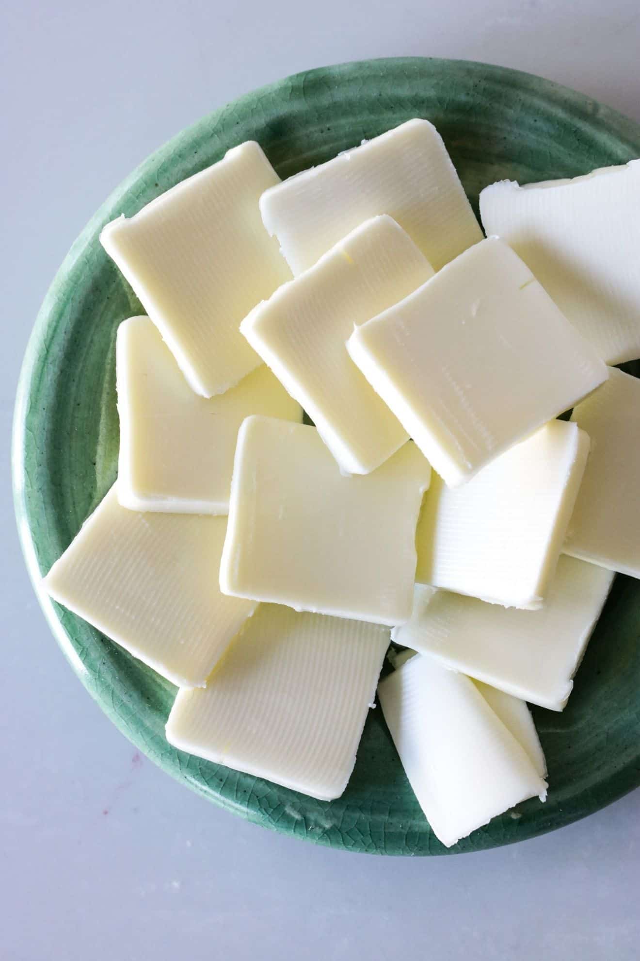 This is an overhead image of a light green plate on a white counter. On the plate is butter cut into squares.
