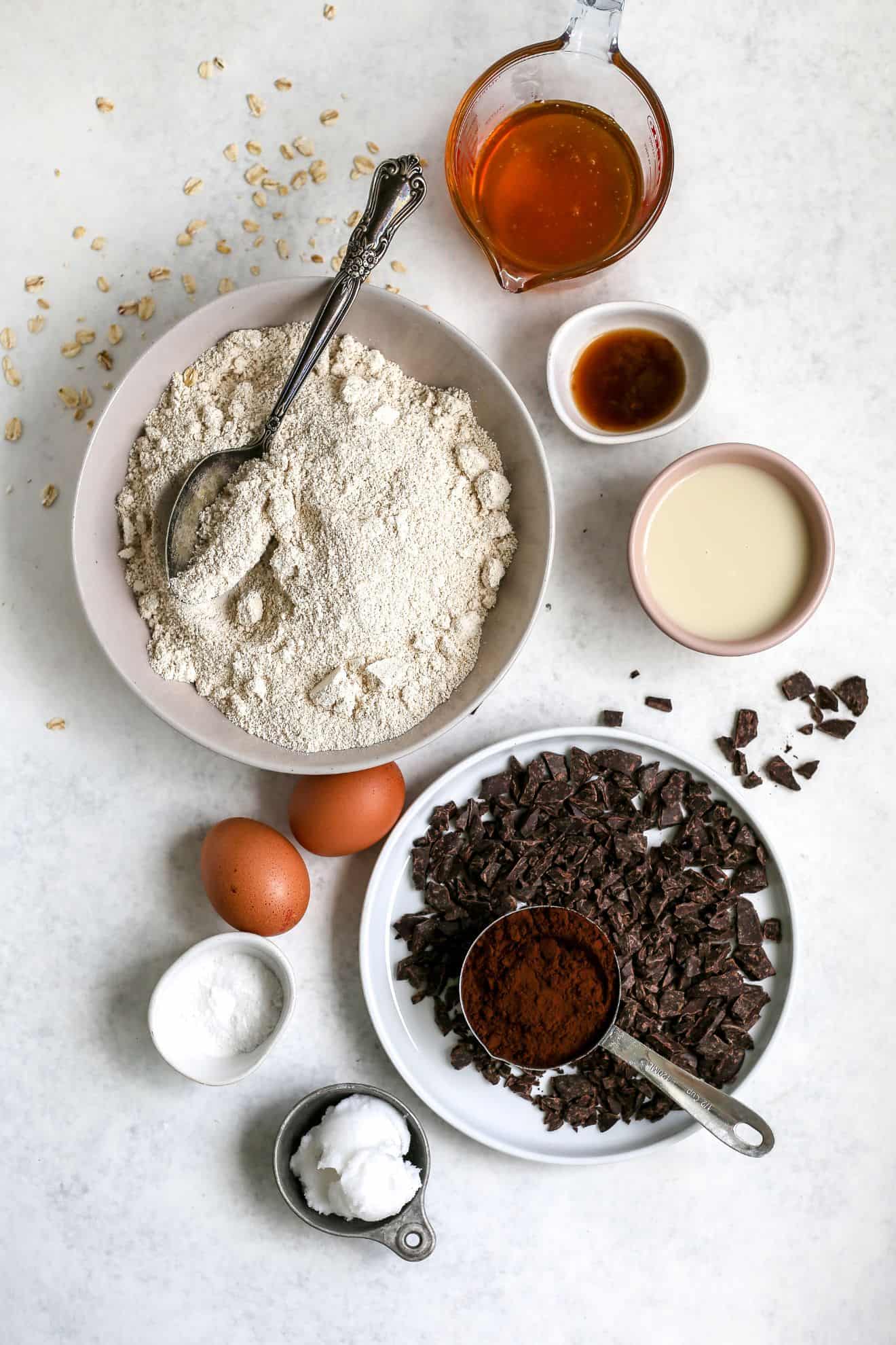 This is an overhead image of ingredients to make chocolate muffins. Bowls and plates of individual ingredients sit on a light grey surface.