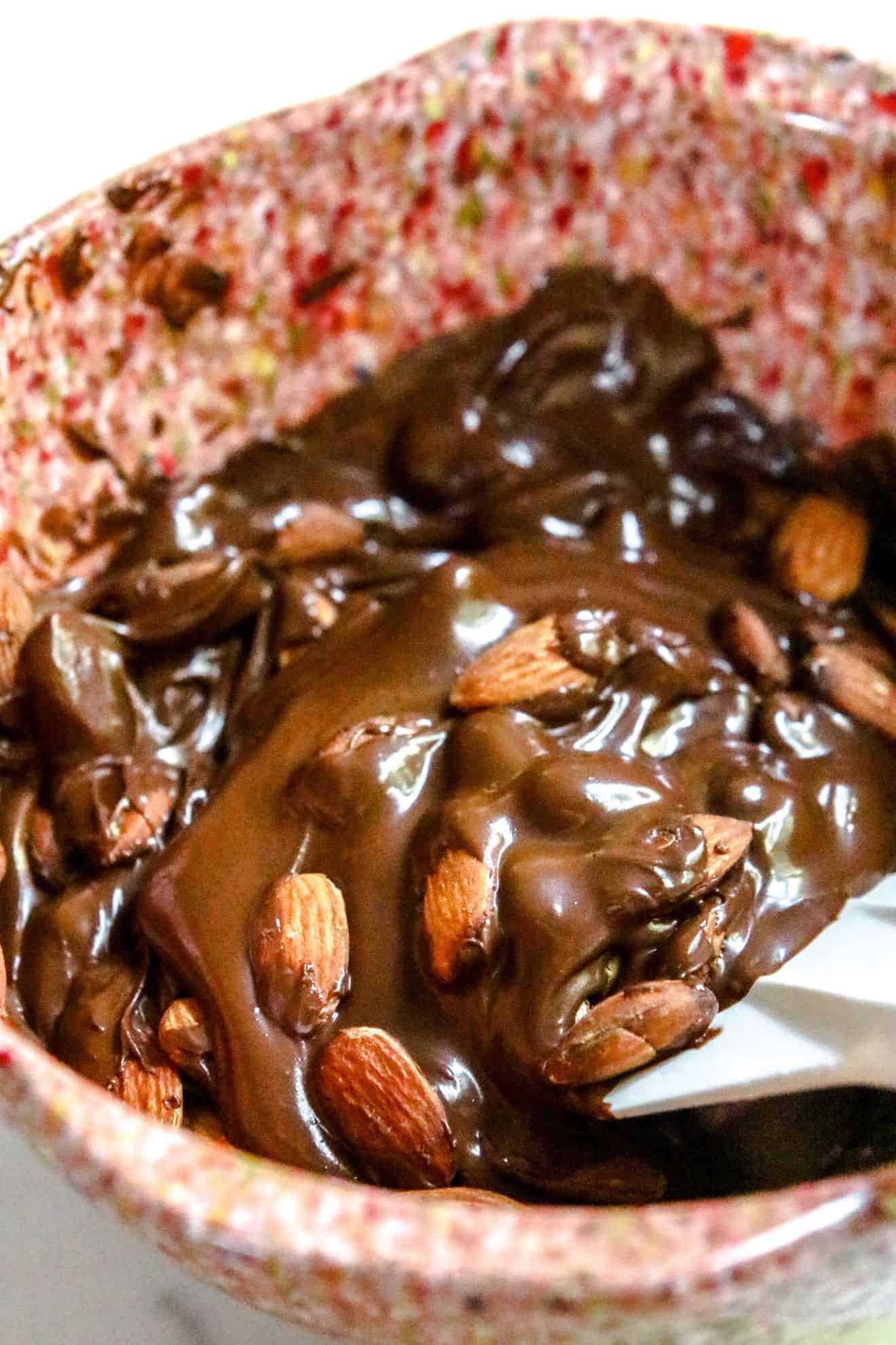 This is a side view of melted chocolate folded with almonds. The melted chocolate is in a pink speckled mixed bowl sitting on a white marble counter.
