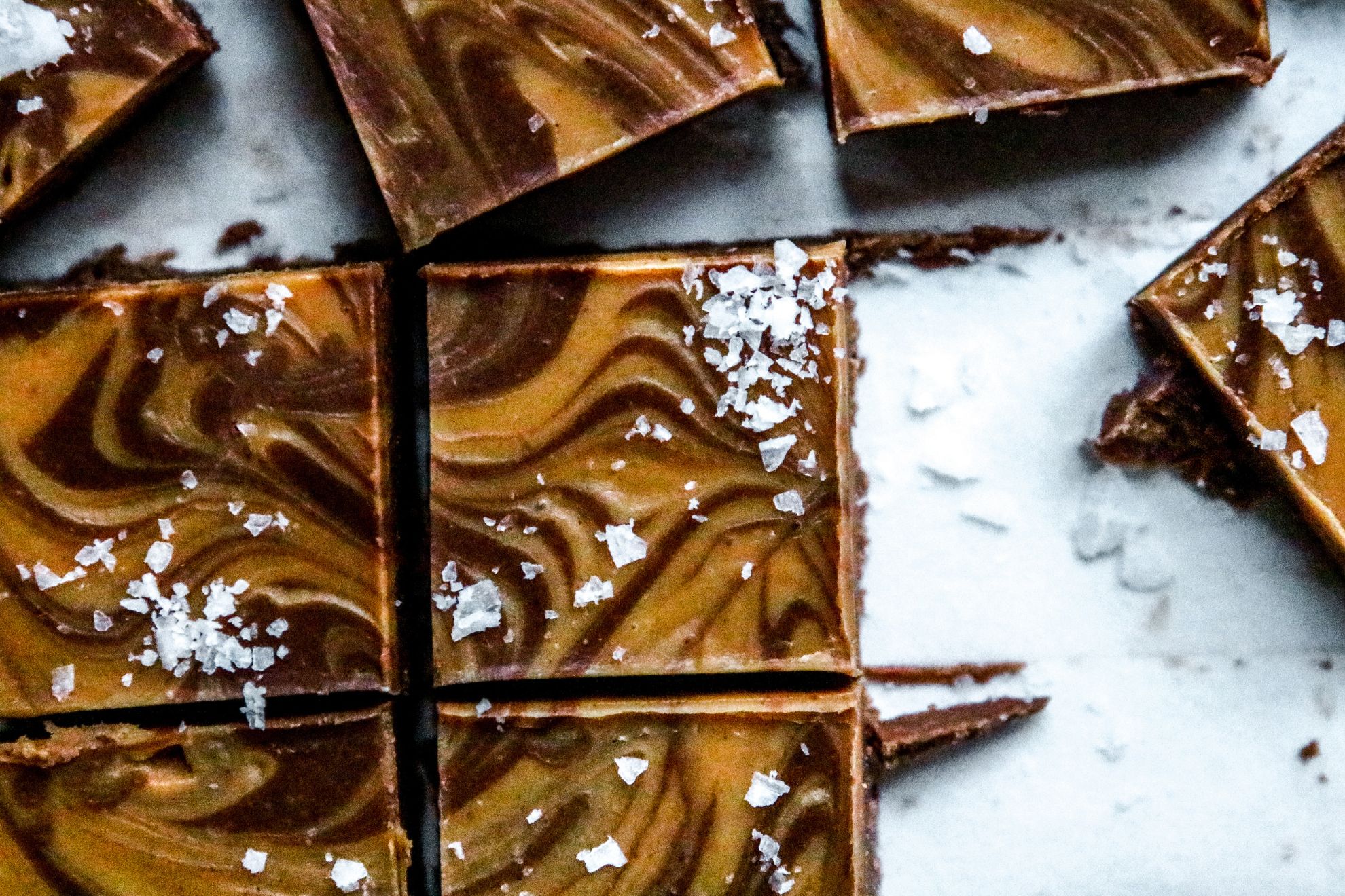 This is an overhead image of chocolate and peanut butter swirl fudge cut into squares. The fudge squares are topped with salt and are on a piece of white parchment paper.