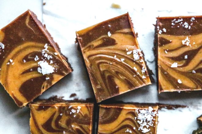 This is an overhead image of chocolate and peanut butter swirl fudge cut into squares. The fudge squares are topped with salt and are on a piece of white parchment paper.