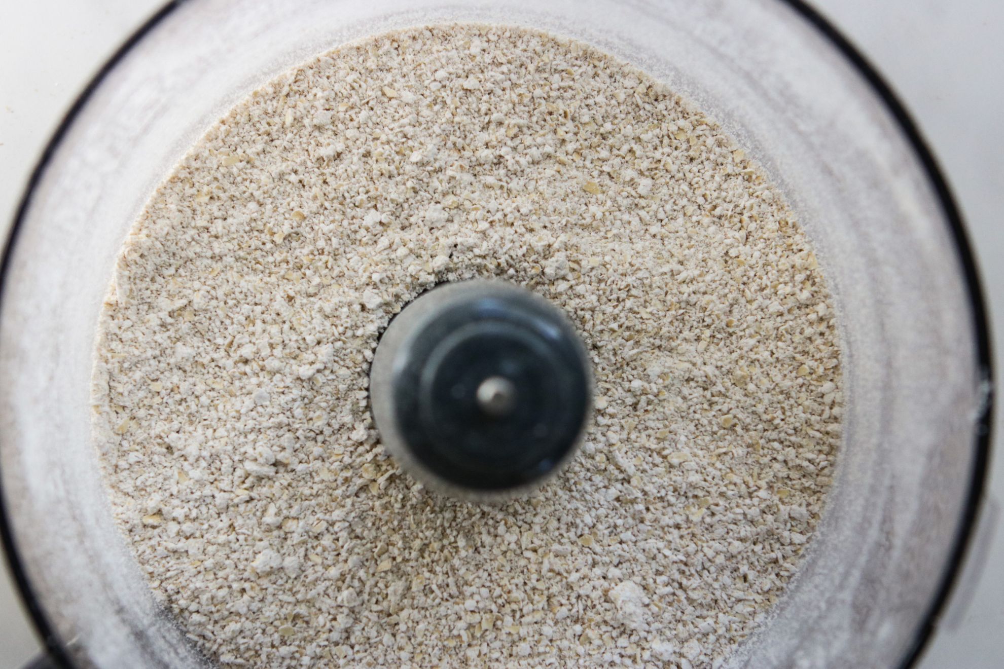 This is an overhead image looking down into a food processor. There is ground up oats in the food processor.