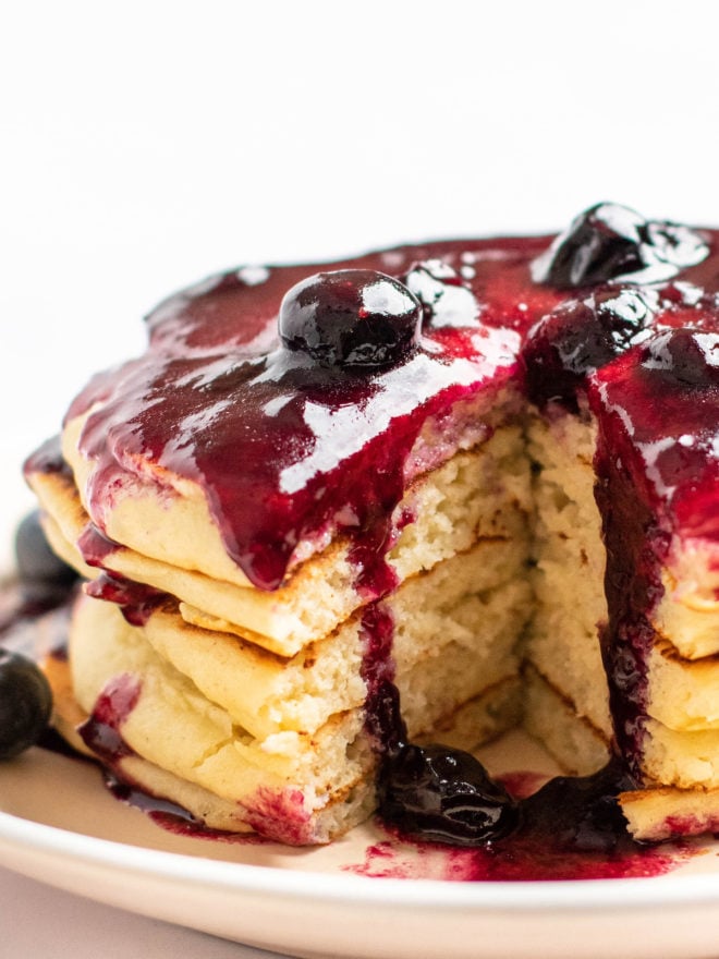This is an overhead image of a stack of pancakes with blueberry glaze on top. The pancakes sit on a white plate on a white background. 