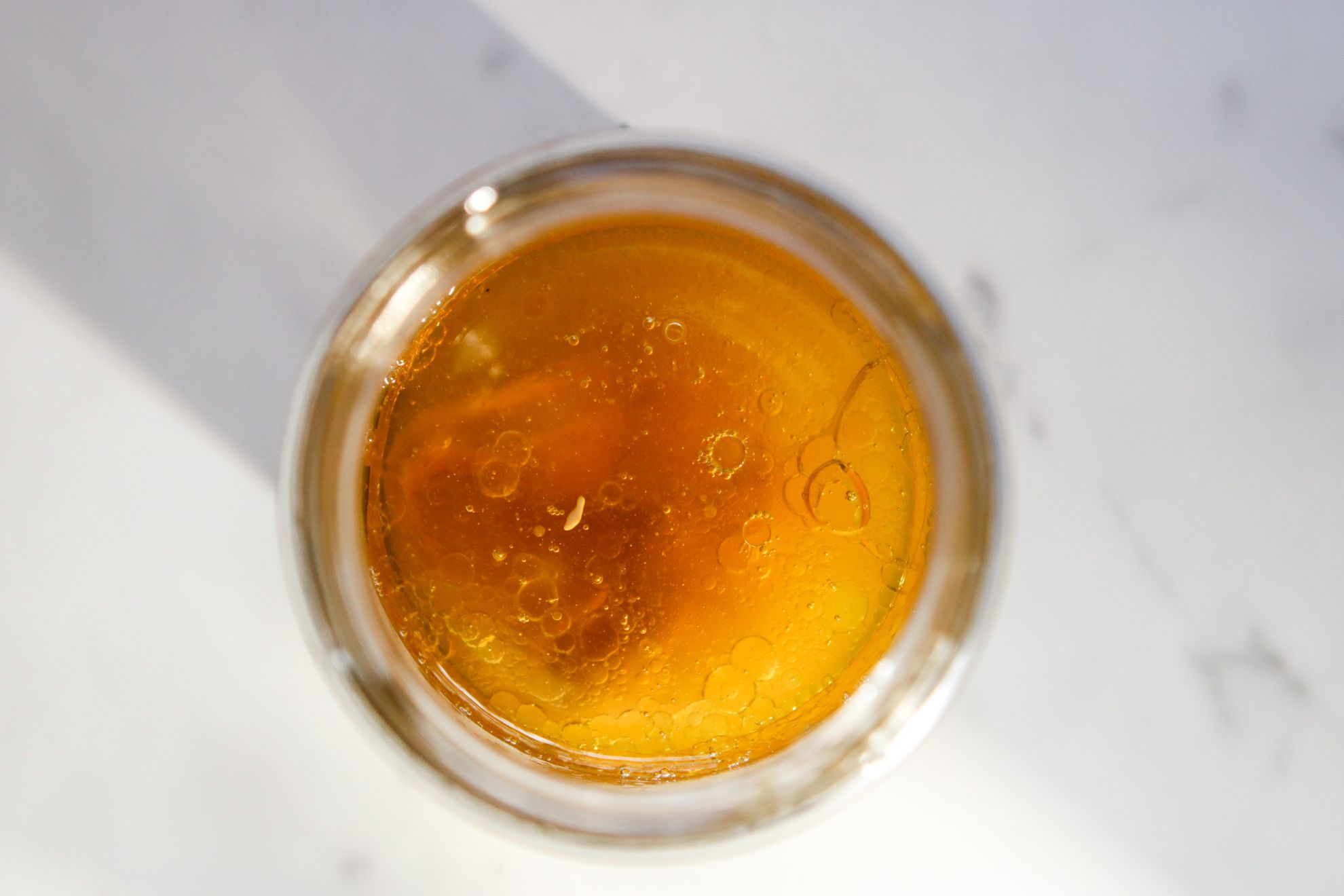 This is an overhead image of a glass jar filled with amber color liquid. The jar sits on a white marble counter.