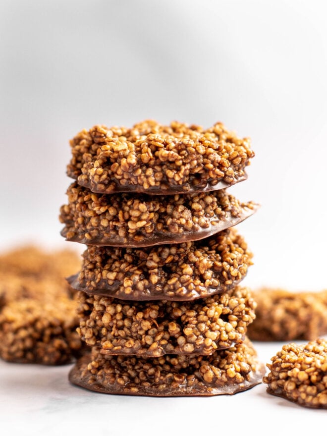 This is a vertical image of a stack of five chocolate quinoa crisps piled on a white counter. More crisps are to the side of the stack and blurred in the background.