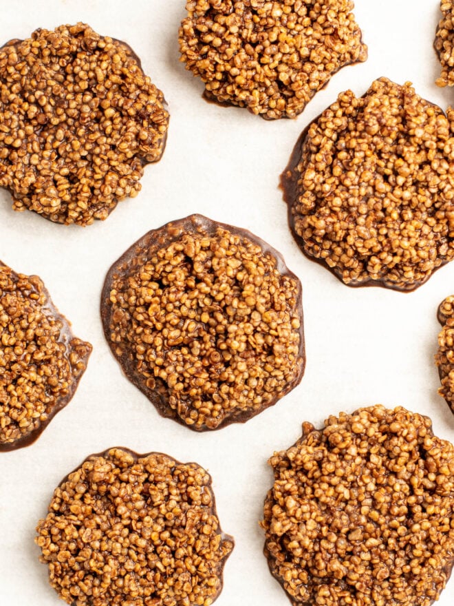 This is a vertical overhead image of chocolate quinoa cookies on a white surface. There are a couple full crisps in view but others are partially shown around the full crisps, cut off at the edge of the image.