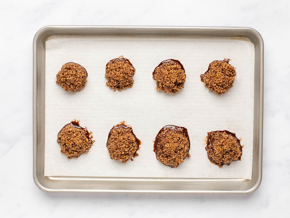 This is a horizontal image of chocolate quinoa mounds on a baking sheet with parchment paper. The baking sheet sits on a white marble surface.