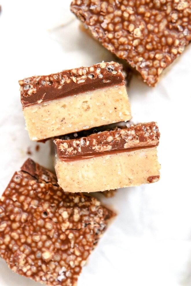 This is an overhead vertical image looking down onto two banana bites leaning on their sides to reveal two layers. The bottom layer is a light beige color and the top layer is a hardened chocolate with crispy quinoa. Two more banana bites are on either side of the centered two. One is to the top right corner and the other is to the bottom left corner of the image.
