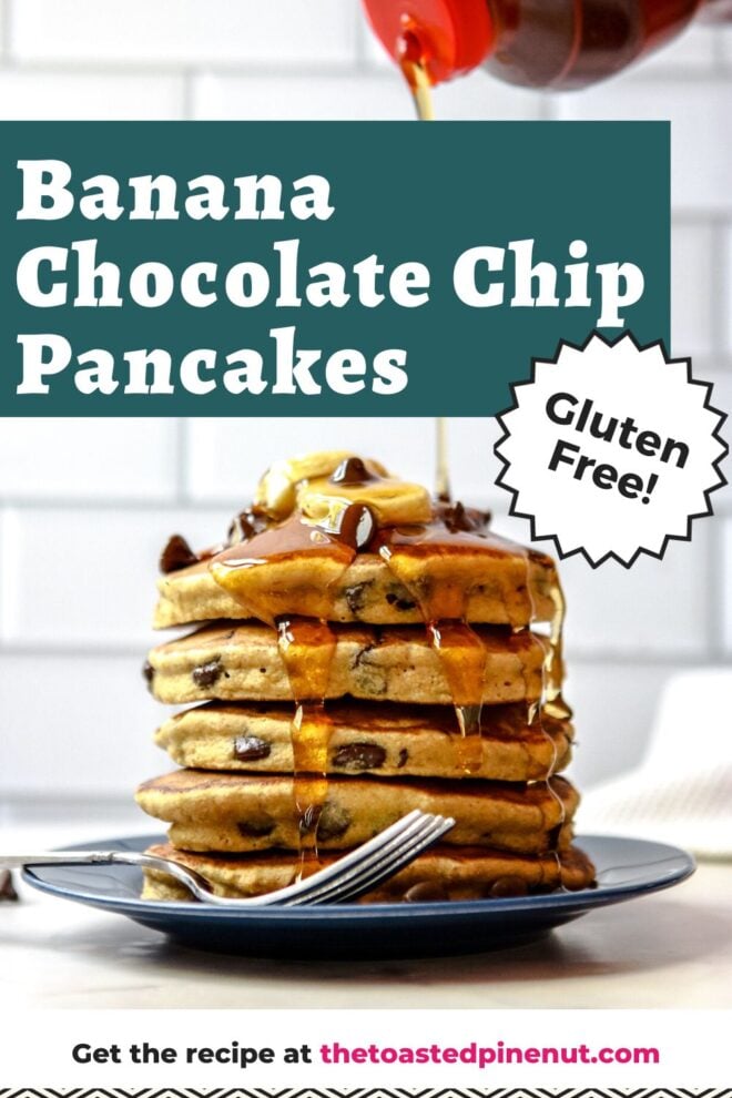 This is a vertical image of a side view of a stack of chocolate chip pancakes. The stack sits on a dark blue plate with a fork at the bottom of the stack leaning against the side of the plate. The plate sits on a white surface with white subway tile in the background. The stack of pancakes is topped with sliced banana and chocolate chips. A syrup bottle with a red lid is coming from the top of the image and pouring syrup on top of the pancakes. The syrup drips down the sides of the pancake stack. Text overlay reads "banana chocolate chip pancakes gluten free! get the recipe at thetoastedpinenut.com"