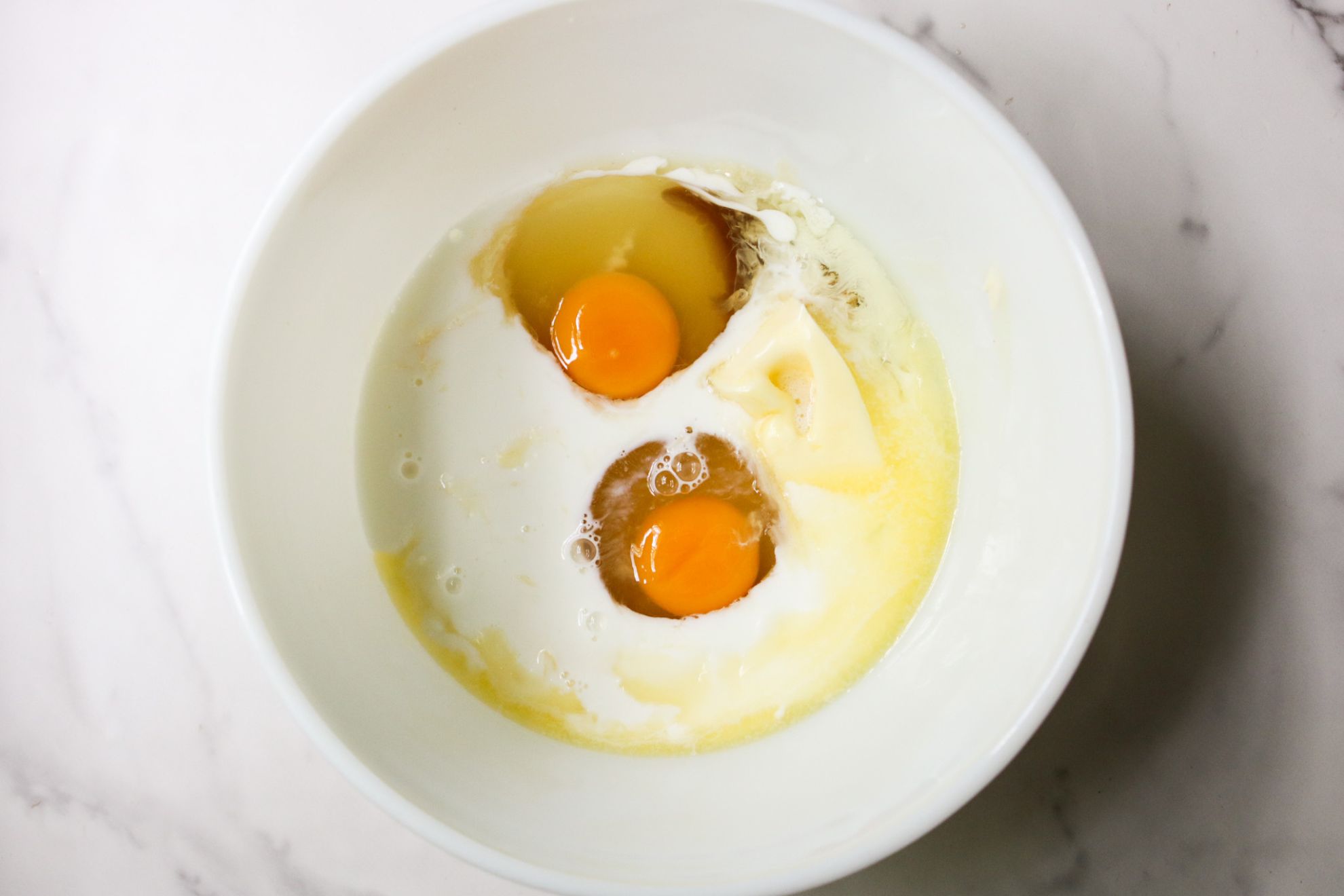 This is an overhead horizontal image of a large white bowl with milk, eggs, and melted butter in it.