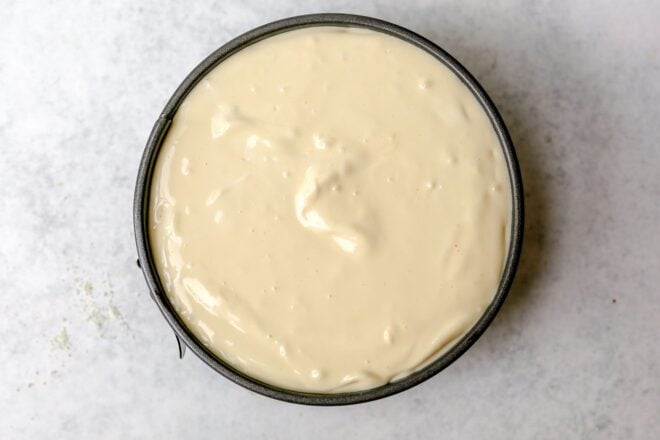 This is an overhead horizontal image of a round springform pan on a light grey surface. In the pan is raw cheesecake batter.