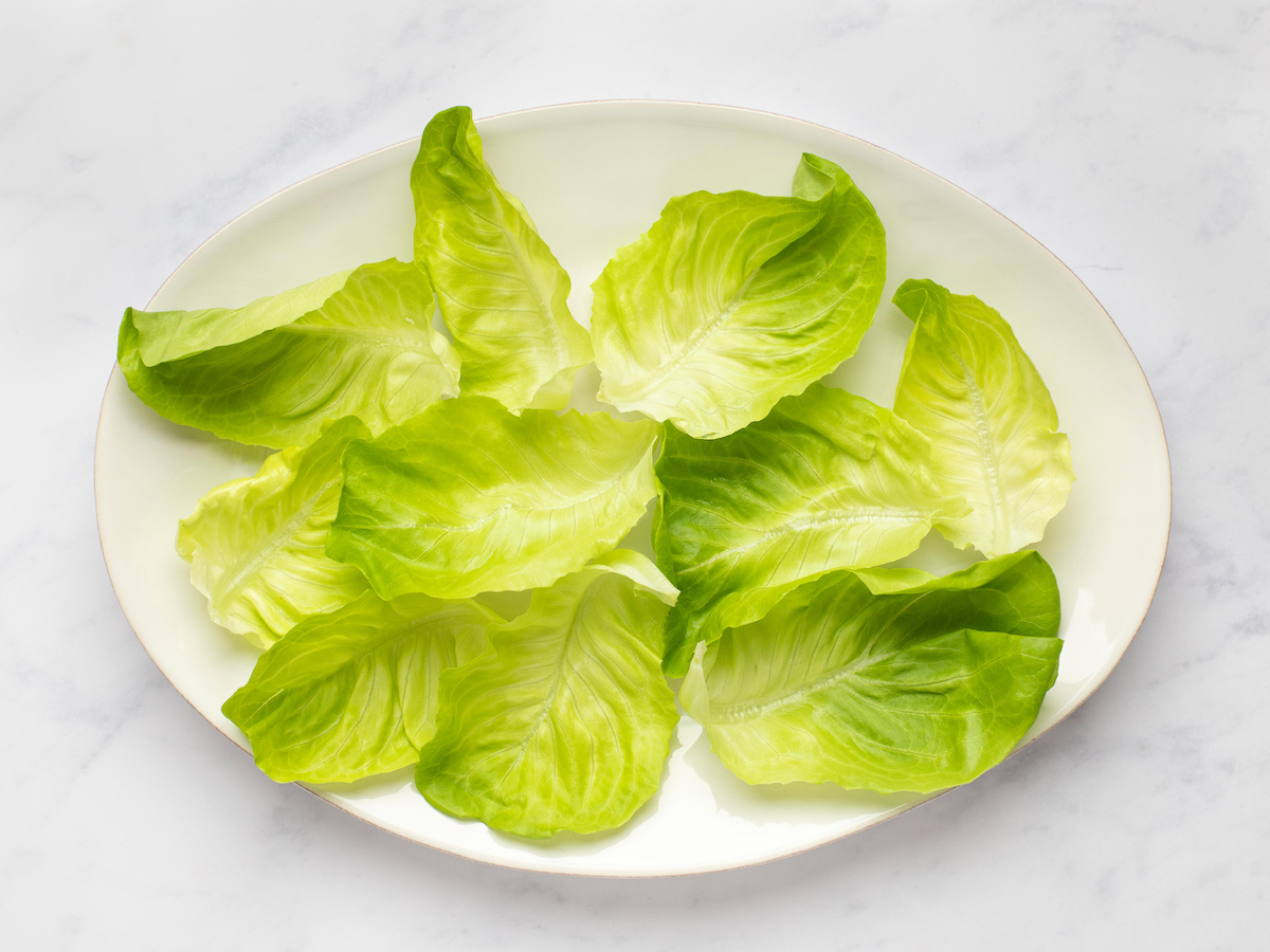 This is an overhead horizontal image of a large white oval plate with empty lettuce leaves on it. The plate sits on a white marble surface.