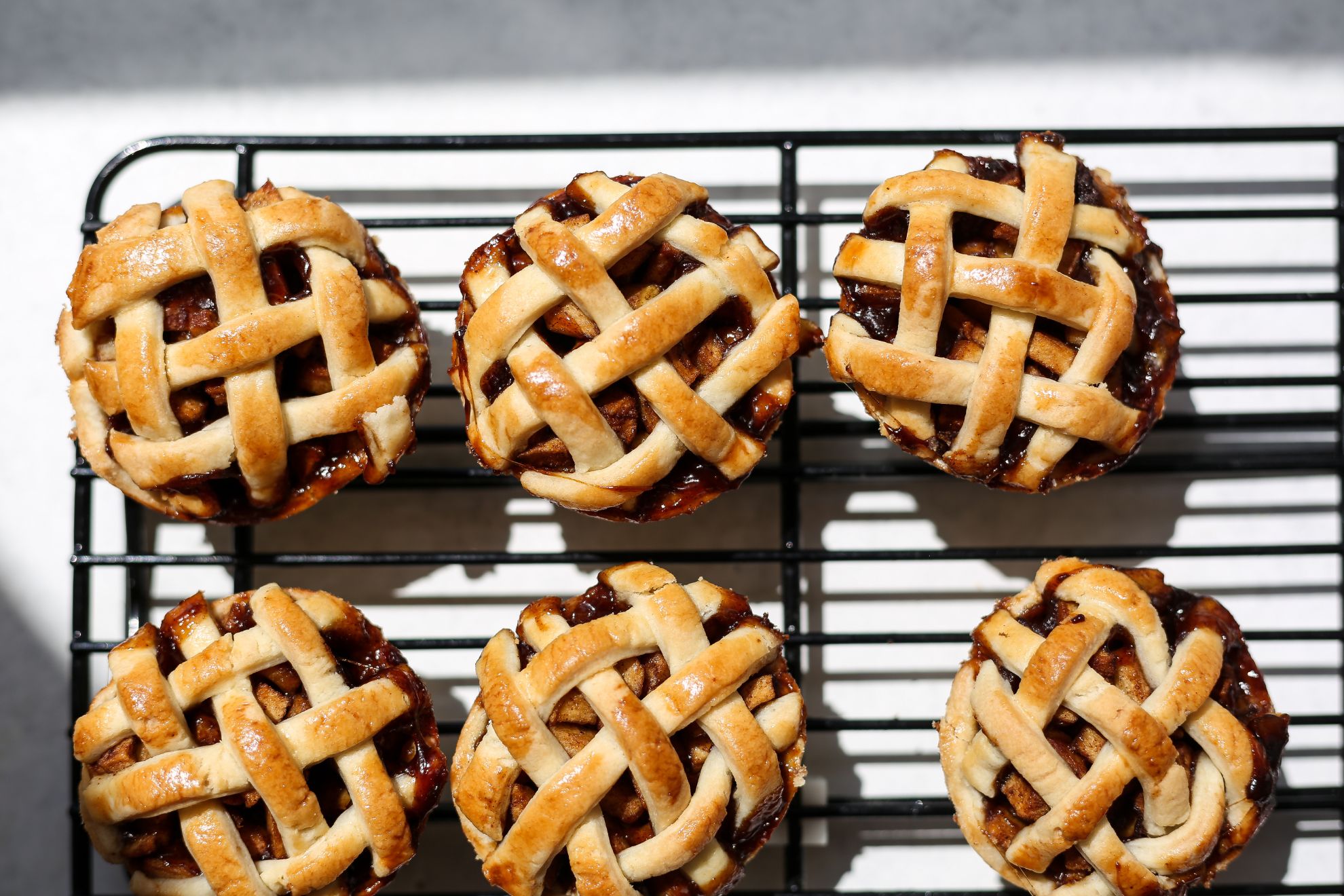 This is a horizontal overhead image of a cooling rack with six mini lattice topped pies on it. The cooling rack is on a white surface.