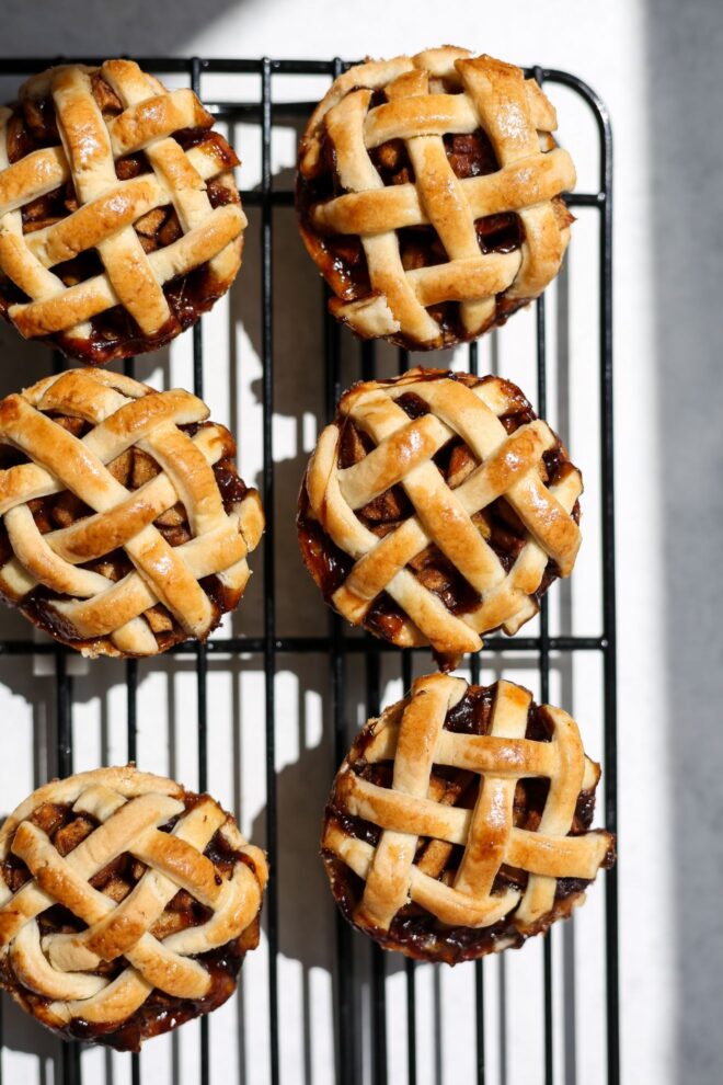 This is a vertical overhead image of a cooling rack with six mini lattice topped pies on it. The cooling rack is on a white surface.