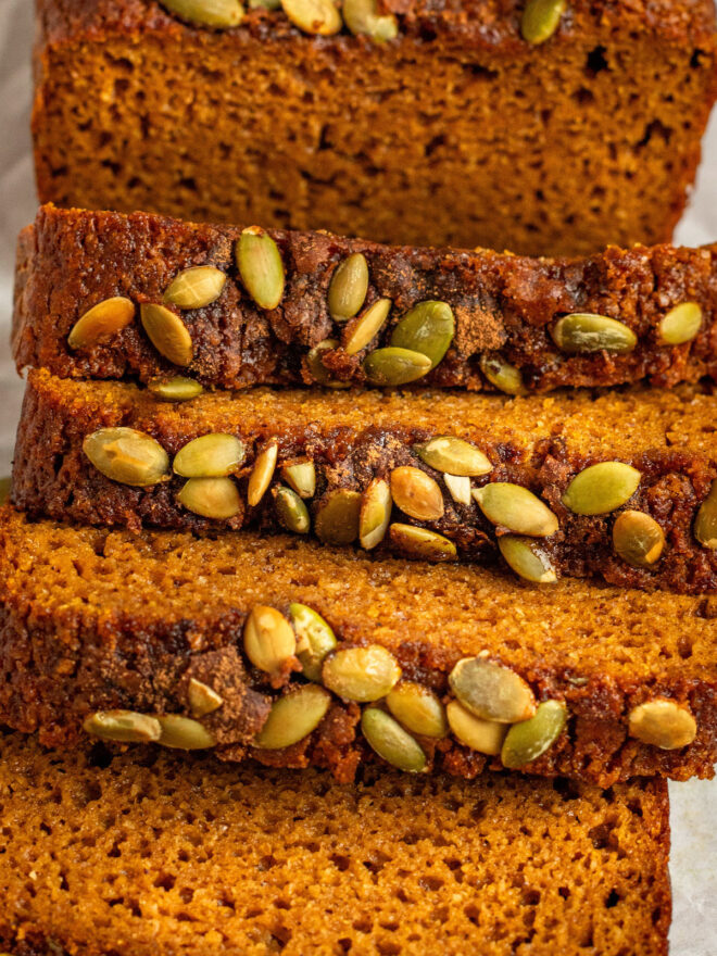 This is a vertical closeup of slices pumpkin bread showing the fluffy texture. The slices are topped with green pumpkin seeds.