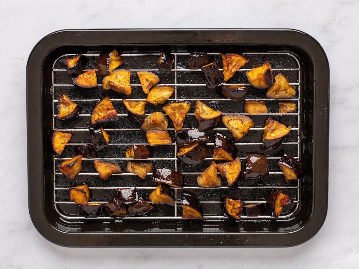 This is an overhead horizontal image of triangles of air fried eggplant spread out in an even layer on an air fryer try. The tray sits on a white marble surface.