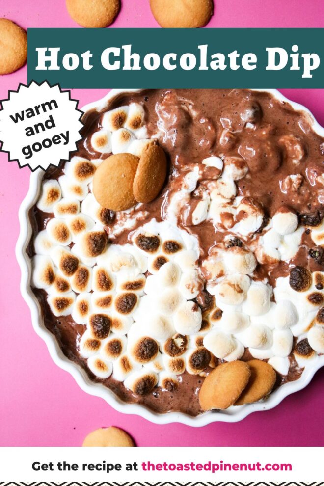 This is an overhead vertical image of a white ceramic scalloped pie dish on a deep pink surface. In the pie dish is a melty, gooey chocolate topped with toasted marshmallows. Nilla wafers are scattered on the pink surface and a few are dipped into the chocolate dip. Text overlay reads "hot chocolate dip warm and gooey."