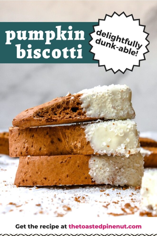 This is a vertical image looking at a stack of three pumpkin biscotti from the side. The stack sits on a white parchment paper with lots of crumbs on it. The biscotti is dipped in white chocolate and has white sugar sprinkles on it. More biscotti is blurred in the background against a marble backdrop. Text overlay reads "pumpkin biscotti delightfully dunk-able!"