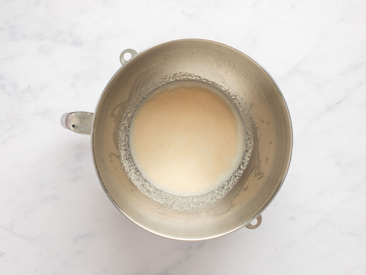 This is an overhead horizontal image of a silver mixing bowl with milk and yeast in it. The bowl sits on a white marble counter.