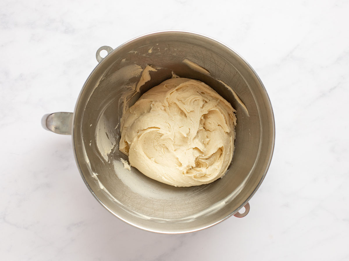 This is an overhead horizontal image of a silver mixing bowl with sticky dough in it. The bowl sits on a white marble counter.
