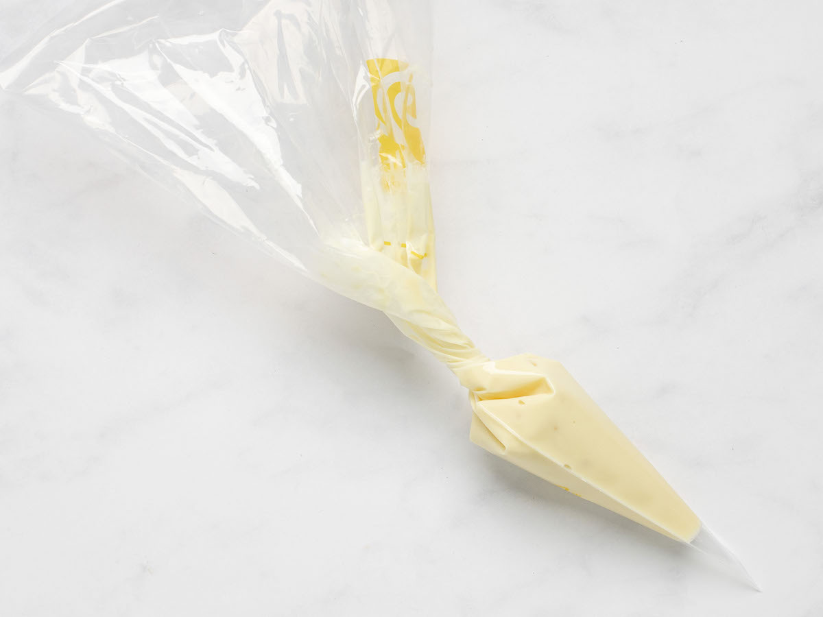 This is an overhead horizontal image of a clear plastic piping bag filled with white chocolate. The baggie sits on a white marble surface.