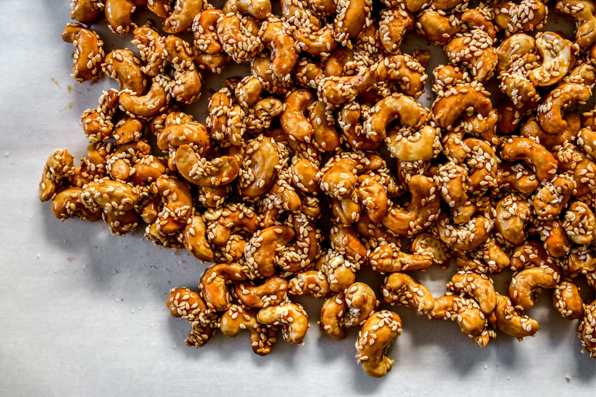 This is an overhead horizontal image of cashews coated with sesame seeds and a caramel coating. The cashews are all very close together and on a white background.